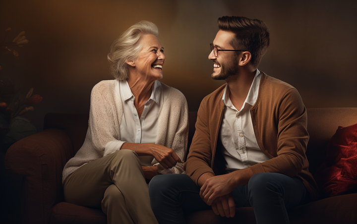 An elderly woman and a man sitting on a couch talking and laughing